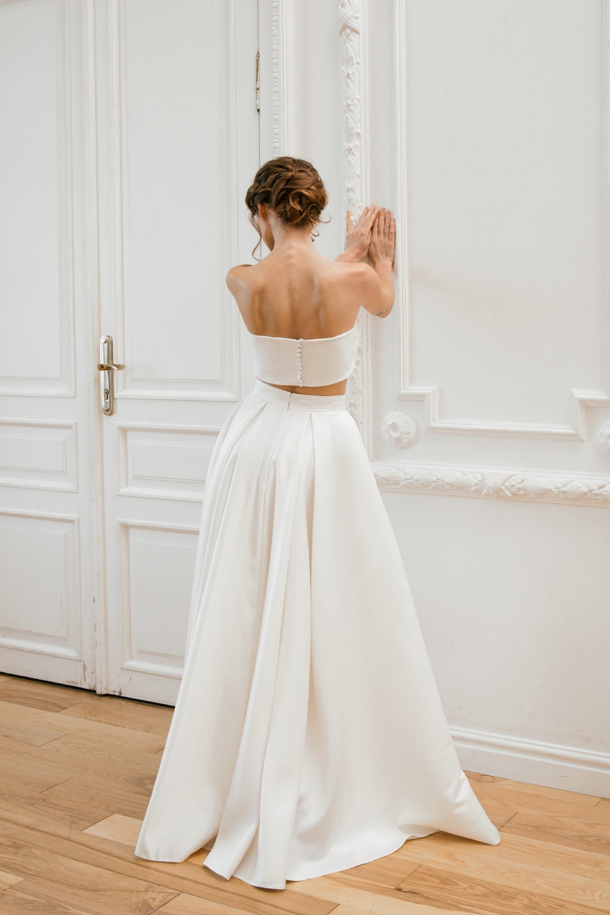 Back view of a two-piece mikado wedding dress with a covered-button crop top and pleated skirt