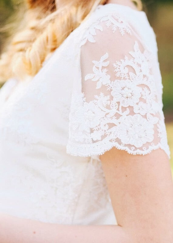 Close-up of Flora's sheer scalloped lace sleeve with floral pattern

