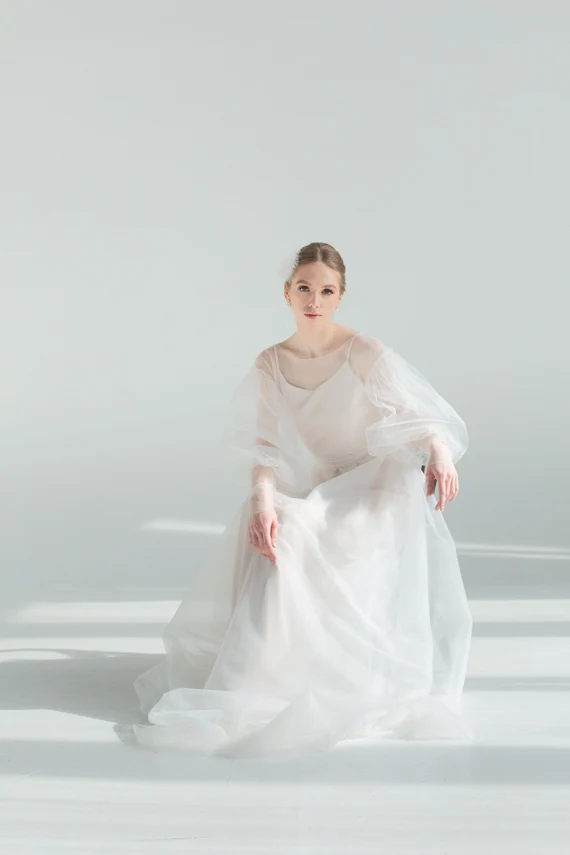 Bride seated in Kosmea sheer tulle wedding dress holding the skirt