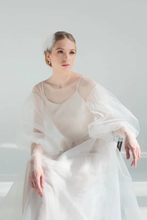 Bride seated in Kosmea wedding dress, sheer tulle sleeve detail
