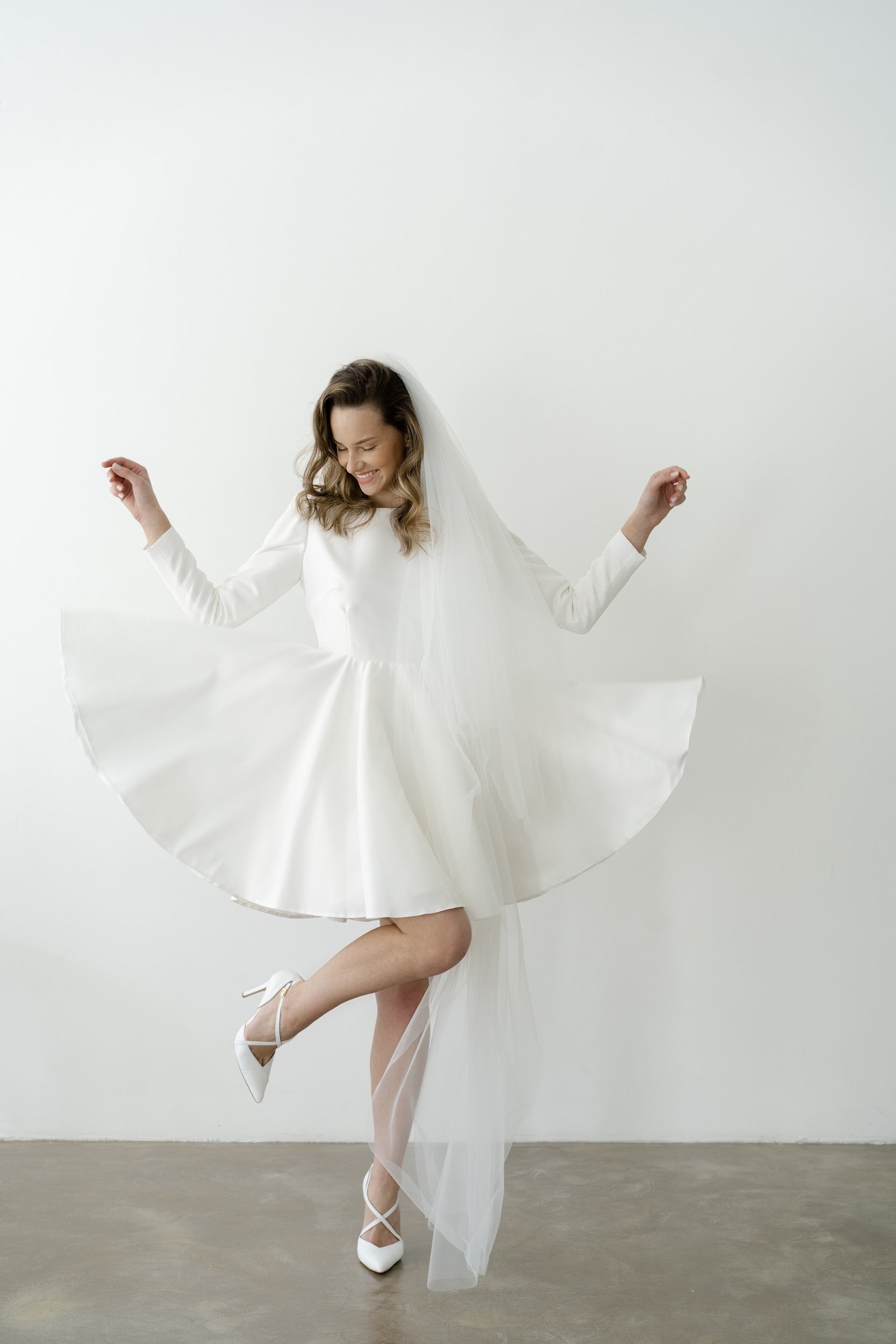 Bride spinning in a short long-sleeve wedding dress with a full circle skirt and veil