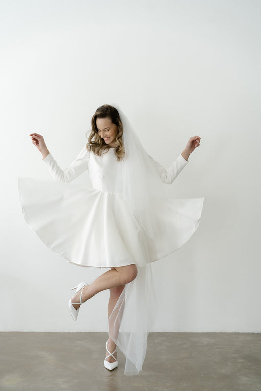 Bride spinning in a short long-sleeve wedding dress with a full circle skirt and veil